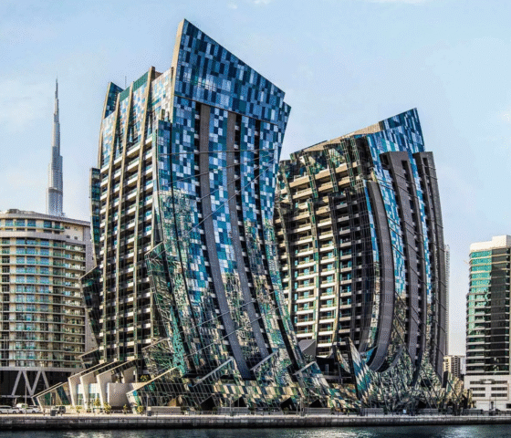Modern architectural towers with fragmented glass facades overlooking a canal, with the Burj Khalifa in the background.