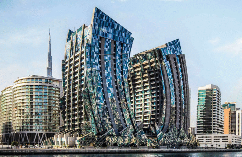 Modern architectural towers with fragmented glass facades overlooking a canal, with the Burj Khalifa in the background.