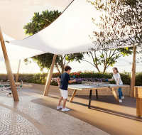 Children playing table tennis in a shaded outdoor recreation area.