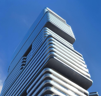 Modern high-rise tower with layered balconies and sleek architectural design against a clear blue sky.