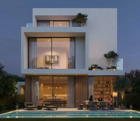 Rear view of a modern villa at Chevalia Estate 2, showing the backyard with a swimming pool and illuminated patio area at dusk.