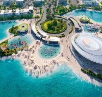 An outdoor leisure hub with water slides, a sandy beach, and various recreational facilities surrounded by clear blue water.