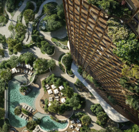 Aerial view of a landscaped garden with winding pathways, swimming pools, sun loungers, and dense greenery beside a modern residential tower.