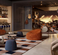 A man playing an acoustic guitar in a stylish music room with a large screen and drum set.