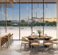 Bright modern dining area with round table and floor-to-ceiling windows overlooking outdoor lounge.