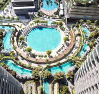 High-rise residential tower with glass balconies overlooking a lagoon and city skyline.