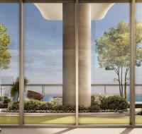 Modern gym with stationary bikes facing a terrace garden, featuring trees, shrubs, and ocean views under clear skies.