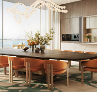 Luxury open-plan dining and kitchen area with a large oval table, orange chairs, and a panoramic sea view.