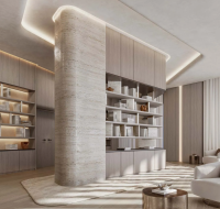 Luxurious modern library/lounge with built-in wooden shelves, recessed lighting, a curved stone column, plush white armchairs, and floor-to-ceiling windows.