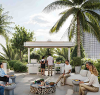Spacious outdoor lounge area with people socializing, barbecue station, and palm trees.